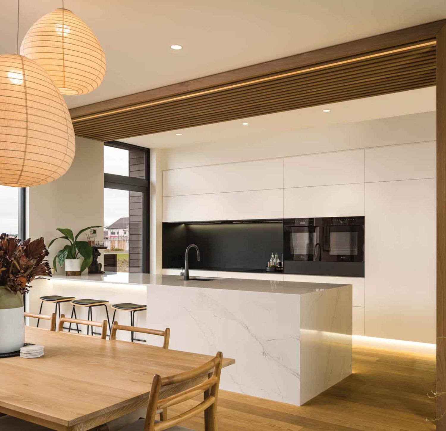 Contemporary kitchen with white marble waterfall island, black splashback and timber ceiling batten detail – Chilton + Mayne architectural designers